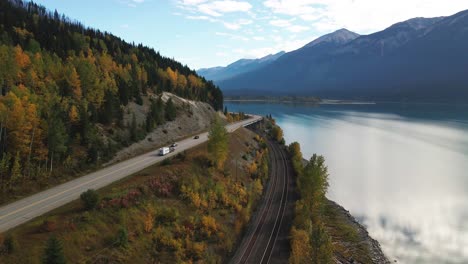 pan-right-aerial-shot-of-Yellowhead-Highway-along-moose-lake-in-Mount-Robson-Provincial-Park-in-autumn-with-yellow-trees-and-mountains-in-the-background-and-cars-driving-on-the-highway-railway-track