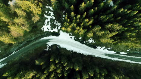 Aerial-top-down-shot-over-a-snow-covered-road-beside-winter-snowy-coniferous-forest-in-Norway-at-daytime