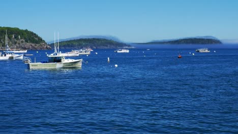 Fishing-Boats-moored-in-blue-waters-of-Bar-Harbor-with-a-light-veil-of-fog-sitting-on-lush-green-hills-in-background