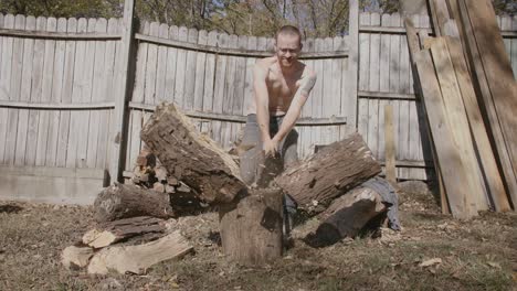 Slow-motion-front-on-wide-angle-of-man-without-shirt-on-splitting-a-large-log-with-a-axe-and-looking-satisfied