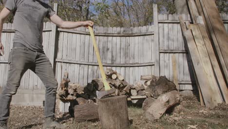 Side-angle-of-a-man-walking-up-to-a-log-in-the-fall-with-an-axe-and-splitting-it