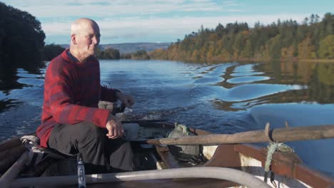 A-mature-man-driving-rowboat-with-outboard-engine-surrounded-by-Autumn-colours