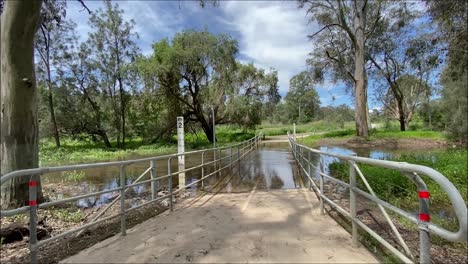 Toma-Deslizante-Suave-De-Derecha-A-Izquierda-De-Un-Puente-Peatonal-Inundado-Sobre-Un-Arroyo-Crecido-Después-De-La-Lluvia-Torrencial-Y-La-Inundación-En-Las-Inundaciones-Australianas-En-Octubre-De-2023