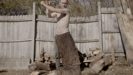 Slow-motion-front-on-wide-angle-of-man-without-shirt-on-splitting-a-log-with-a-axe