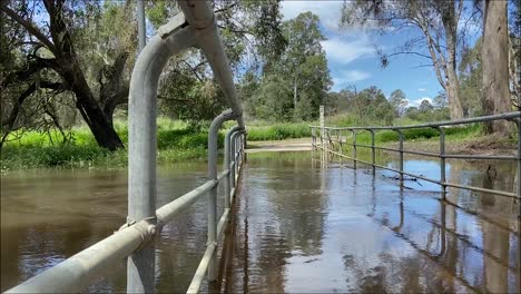 Niedrigwinkelansicht-Durch-Das-Geländer-Mit-Blick-über-Eine-überflutete-Fußgängerbrücke-über-Einen-Angeschwollenen-Bach-Nach-Hochwasserregen-Und-Überschwemmungen-Bei-Den-Australischen-Überschwemmungen-Im-Oktober-2025