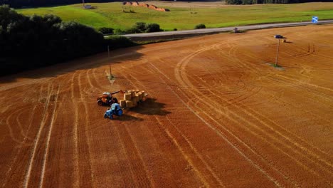 An-aerial-view-of-a-large-industrial-golden-field-with-a-tractor-collecting-hay-bales
