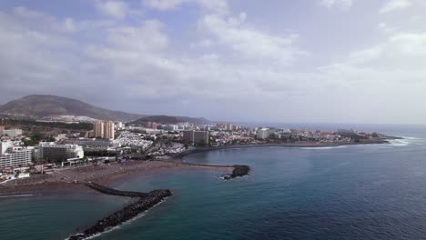 Vista-Aérea-De-Una-Ciudad-Turística-En-Una-Playa-De-Arena-Negra-En-La-Bahía-De-Tenerife