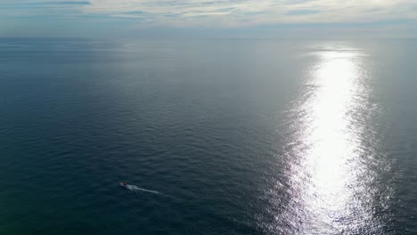 Croatia-Adriatic-sea-sun-setting-and-reflecting-on-surface-small-boat-moving-across-shot-from-drone