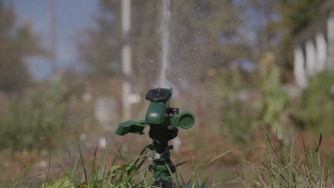 Slow-motion-footage-of-a-sprinkler-watering-the-yard-with-the-background-out-of-focus