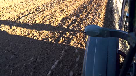 Tractor-driving-on-the-side-of-plowed-field,-view-from-cabin-on-front-wheel