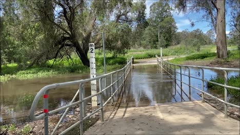 Toma-Deslizante-Suave-De-Izquierda-A-Derecha-De-Un-Puente-Peatonal-Inundado-Sobre-Un-Arroyo-Crecido-Después-De-La-Lluvia-Torrencial-Y-La-Inundación-En-Las-Inundaciones-Australianas-En-Octubre-De-2022