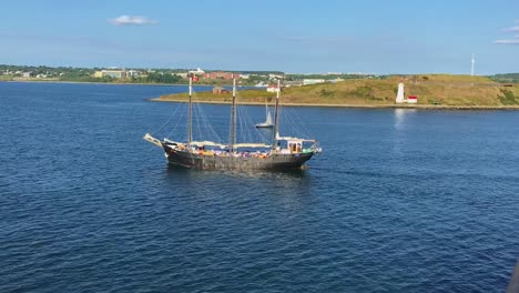 3-mast-Barque-sailing-vessel-crusing-in-harbor-in-front-of-lighthouse-on-Eastern-coast-of-Canada