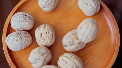 In-a-beautiful-light,-walnuts-fall-into-the-wooden-plate-in-slow-motion,-top-view-and-close-up-shot