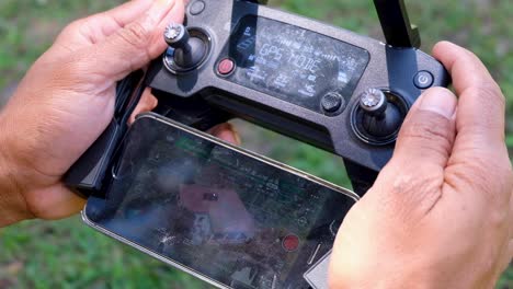 Drone-pilot-person-flying-a-drone-using-a-drone-controller-and-mobile-phone-screen,-close-up-of-hands-operating-camera-equipment