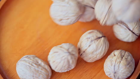 In-a-beautiful-light,-walnuts-fall-into-the-wooden-plate-in-slow-motion,-top-view-and-macro-shot