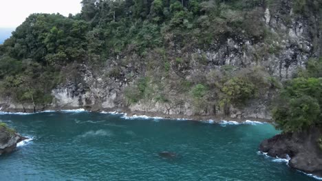 Aerial-dolly-out-revealing-the-true-size-of-a-large-rocky-cliff-at-the-shore-of-Costa-Rica-and-a-large-pelicans-nest-in-front-of-it