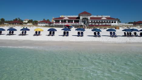Blue-umbrellas-on-Destin-Beach-gulf-coast-panhandle-Florida-white-sandy-beach-clear-emerald-waters-fly-over-with-drone-aerial-view-bright-sunny-day