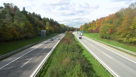 View-over-a-German-Autobahn-with-driving-cars,-framed-by-colorful-trees-of-the-fall-season