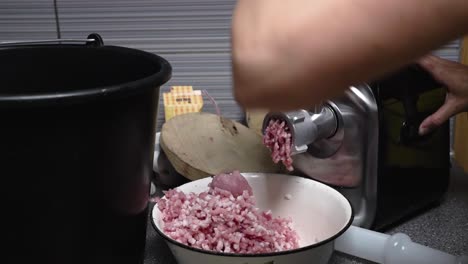 Woman-grinding-pork-for-meatball-mass-with-the-electric-mincer-in-a-kitchen,-slow-motion