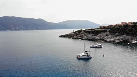 Barcos-Flotando-En-El-Océano-Tranquilo-Con-Hotel-De-5-Estrellas-En-La-Colina-Cerca-De-Paralia-Emplisi-En-Grecia