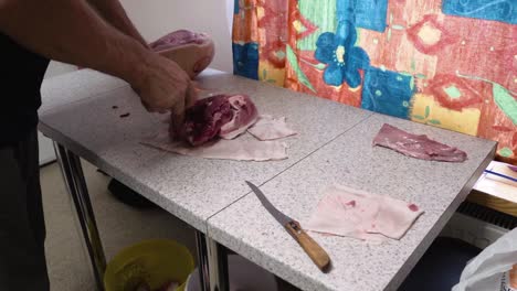 Butcher-cutting-raw-pork-with-knife-in-a-kitchen,-separate-it-from-skin