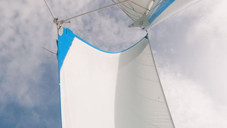 Low-angle-shot-of-genoa-jib-sail-and-mast-against-cloudy-sky,-wind-blowing,-day