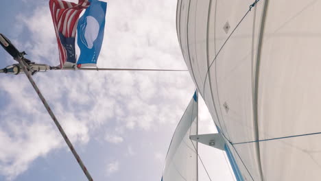 Low-angle-shot-of-saiboat-sails-and-mast-with-flags-blown-by-wind,-day