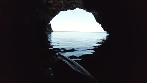 Kayaker-looking-out-to-the-horizon-from-the-inside-of-a-sea-cave-Vis-island,-Adriatic-Sea,-Croatia
