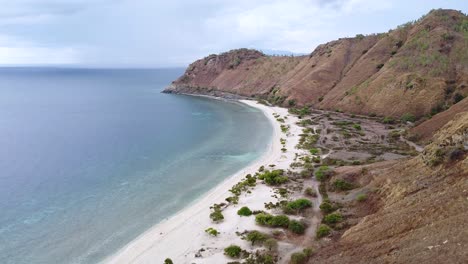 Aerial-drone-rising-over-dry,-arid-brown-mountainous-landscape-during-dry-season-with-beautiful-white-sandy-beach-and-ocean-views-in-capital-Dili,-Timor-Leste-in-Southeast-Asia