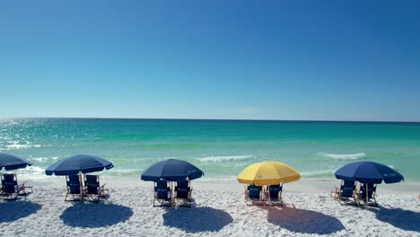 Blaue-Sonnenschirme-Am-Strand-Von-Destin,-Golfküste,-Panhandle,-Florida,-Weißer-Sandstrand,-Klares,-Smaragdgrünes-Wasser,-Fliegen-Mit-Drohnenluftaufnahme,-Heller,-Sonniger-Tag
