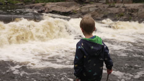 Little-boy-standing-at-the-edge-of-a-river-watching-the-white-water-rapids