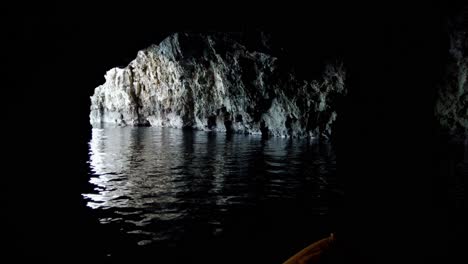 Kayaker-coming-out-of-a-natural-sea-cave,-revealing-the-horizon-through-the-opening,-Vis-Island,-Adriatic-Sea,-Croatia