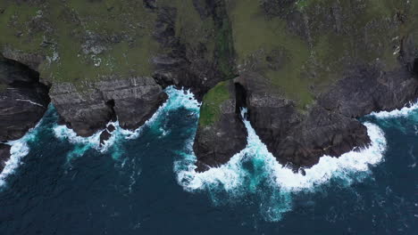 Cinematic-tilting-upward-drone-shot-of-the-ocean-crashing-against-the-edge-near-Keem-Beach,-Ireland