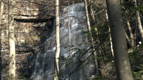 Langsamer-Blick-Auf-Großen-Wasserfall-Im-Wald-Mit-Zweigen-Im-Vordergrund,-4k