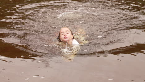 A-happy-little-girl-swimming-in-a-lake-during-a-summer-vacation,-slow-motion