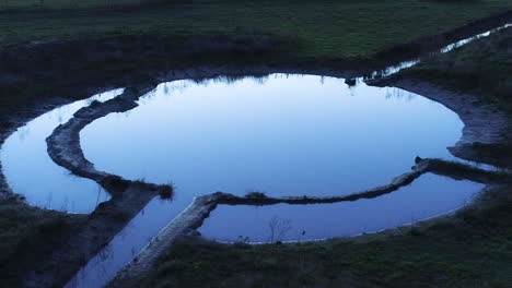 Cinematic-view-of-bird-flying-above-a-circular-water-catchment-during-last-light-hours-like-a-spell-being-cast-over-body-of-water