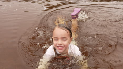 Joyful-little-girl-swimming-and-splashing-in-a-muddy-river,-slow-motion