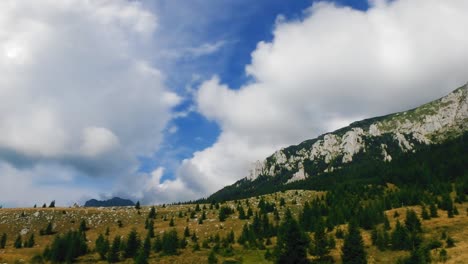 Timelapse-of-clouds-passing-over-a-meadow,-a-pine-forest,-and-a-mountain-cliff