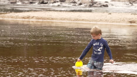 Little-boy-collecting-water-in-a-bucket-from-a-lake,-slow-motion