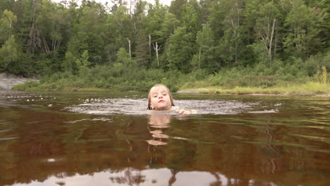 Niña-Feliz-Nadando-Hacia-La-Cámara-En-Un-Lago-Del-Norte-De-Ontario,-Cámara-Lenta