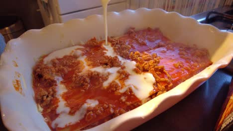 Bechamel-Sauce-Being-Poured-On-Top-Of-Hot-Bolognese-Inside-Lasagne-Dish-With-Cheese-Being-Sprinkled-After