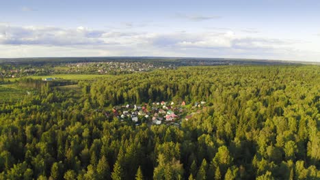 Flight-Above-Sunlit-Broadleaf-Woodland-And-Small-Village-In-A-Forest-Glade