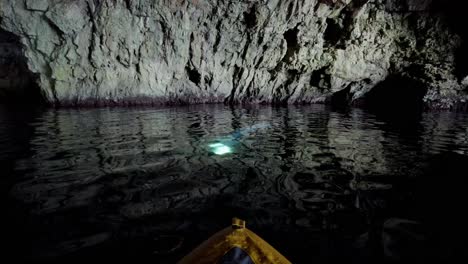 Kayaker-observing-and-moving-towards-a-beam-of-light-in-the-water-inside-a-sea-cave,-Vis-island,-Adriatic-Sea,-Croatia