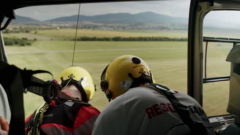 Two-rescuers-with-yellow-helmet-hovering-in-rescue-helicopter-with-open-door