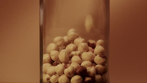 Slow-motion-of-falling-hazelnuts-into-glass-Jar---light-brown-background