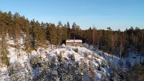 Traditional-Norwegian-Wood-Cabin-In-Winter-Forest---aerial-drone-shot
