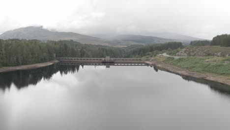 Flying-backwards-looking-at-Laggan-Dam,-located-on-the-River-Spean-south-west-of-Loch-Laggan-in-the-scottish-highlands
