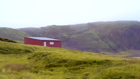 Pintoresca-Cabaña-Roja-Solitaria,-Exuberantes-Campos-Verdes-En-Las-Tierras-Altas-De-Islandia