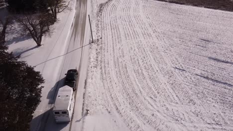Vehicle-tow-horse-trailer-on-icy-rural-road,-aerial-drone-shot