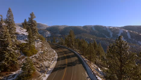 Aerial-of-road-curving-around-bend-in-the-mountains-of-Lake-Tahoe,-Nevada-on-a-beautiful-winter-day